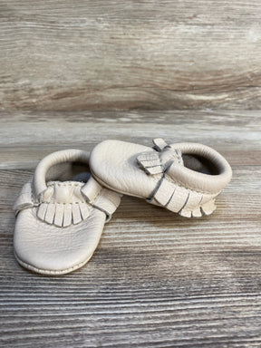 Beige leather baby moccasins with fringe on a wooden background