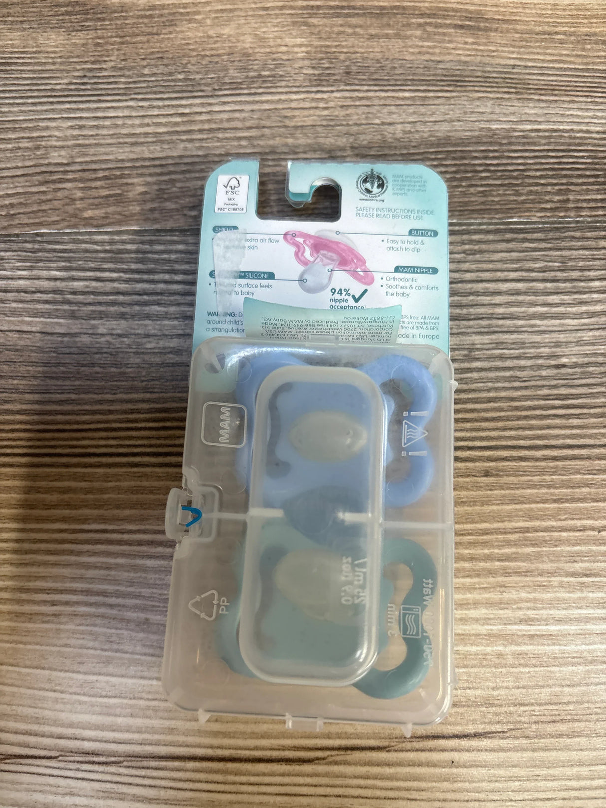 Two blue silicone baby pacifiers in plastic case on wooden surface, orthodontic design