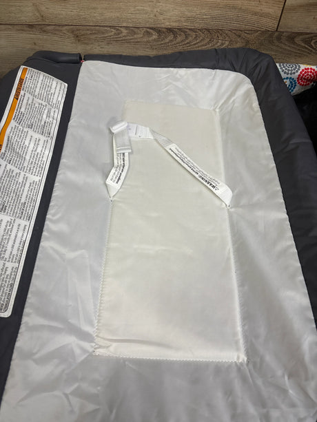 Top view of Baby Trend Lil Snooze Playard Deluxe II nursery center showcasing interior mattress pad and safety strap with wood floor background