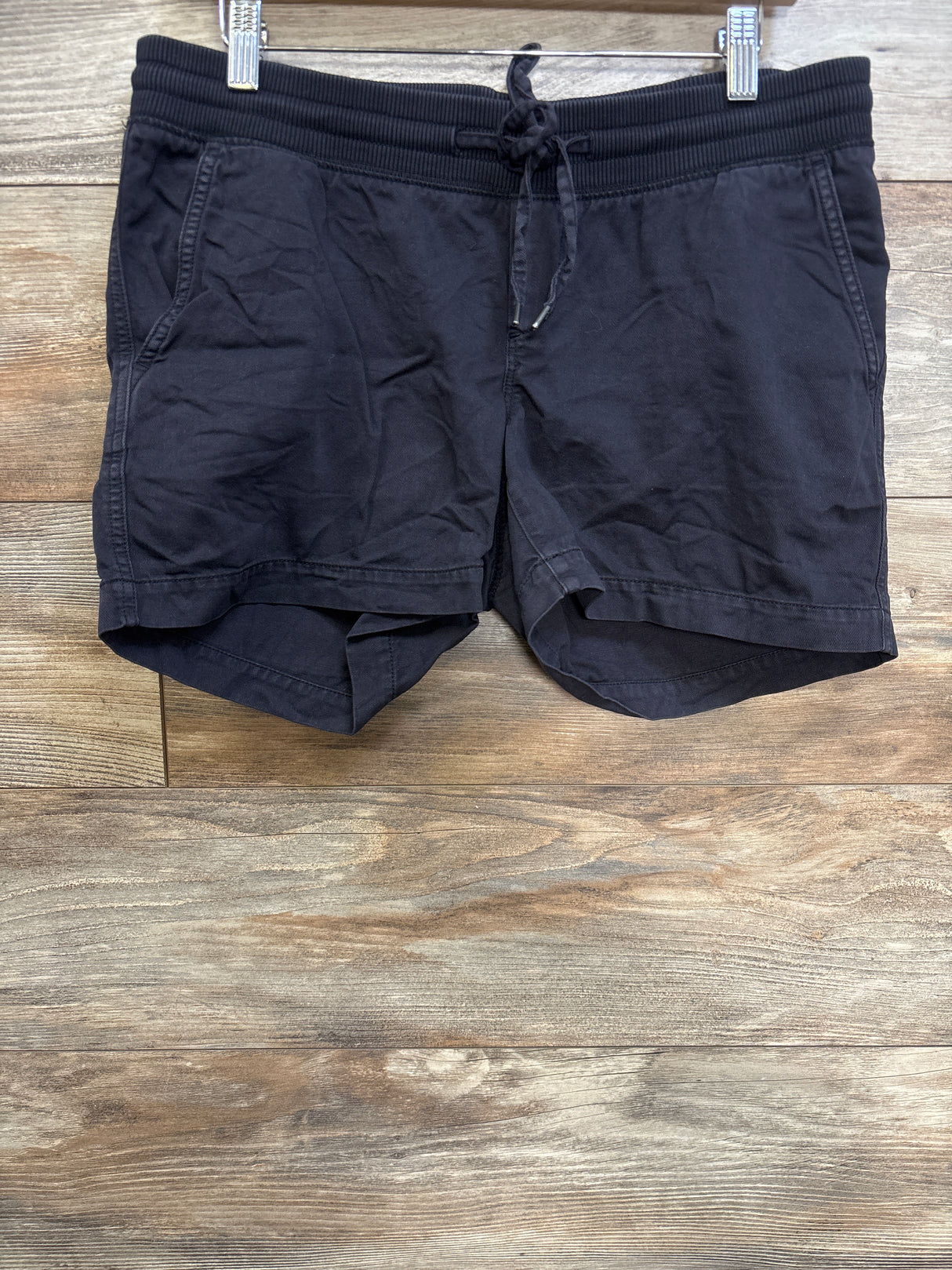 Front view of Gap maternity drawstring shorts in black with elastic waistband, drawstring, and front pockets on wood background