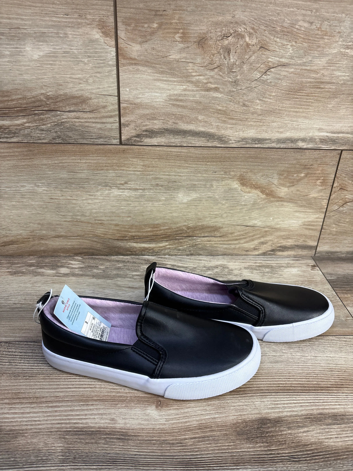 Three-quarter view of Cat & Jack Hailey toddler slip-on sneakers, black with elastic sides and white sole on white background