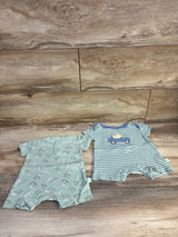 Two baby boy rompers, one with dinosaur print and one blue striped with truck, on wood background.