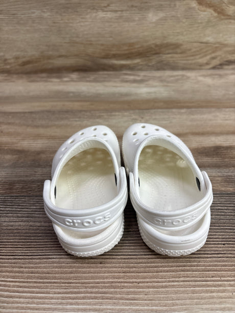Front view of white Crocs Classic Clogs showcasing ventilation holes and heel straps on a wood-grain surface
