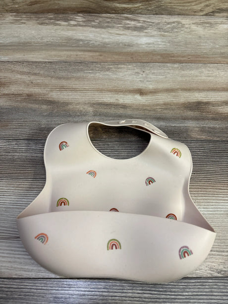 Front view of Mushie silicone baby bib showcasing beige silicone, rainbow print, neck snaps, and catch-all pocket on wood