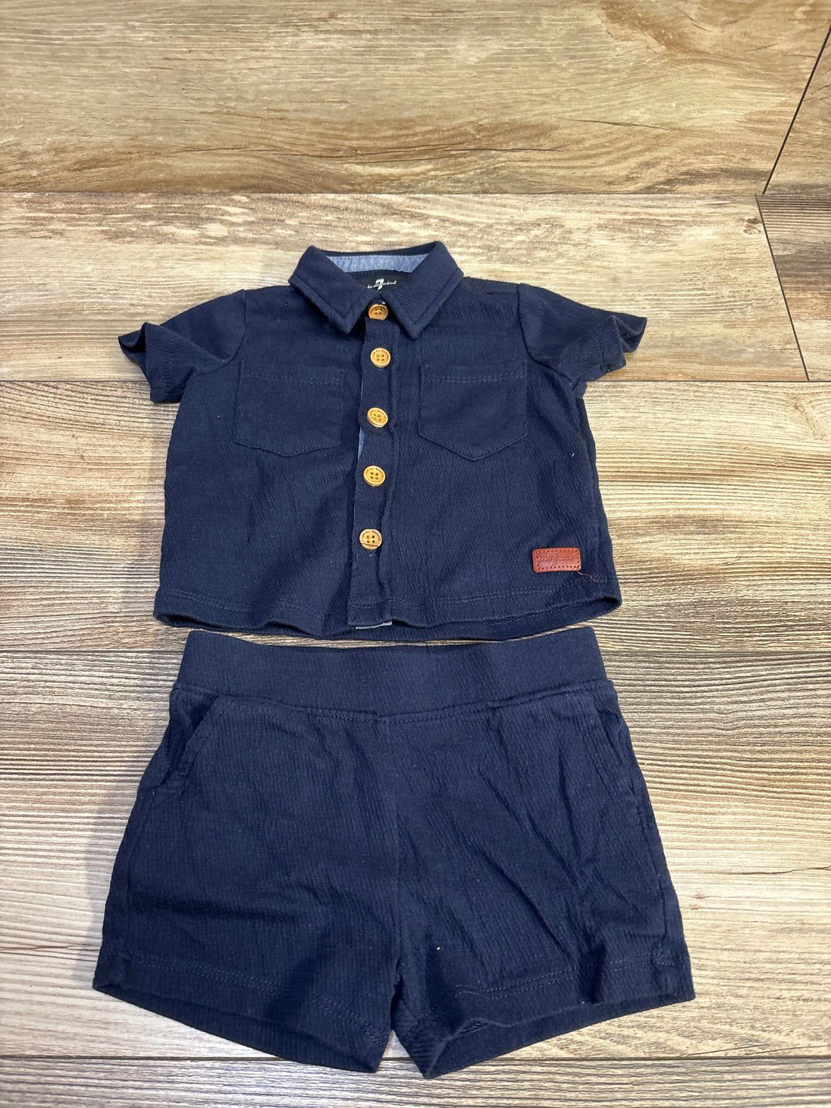 Front view of 7 For All Mankind navy 2pc button-up shirt and shorts set with chest pockets and gold buttons on wood background