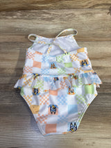 Top-down of girls' Bluey peplum swimsuit with ruffle skirt, crisscross straps, and pastel checkerboard print on light wood