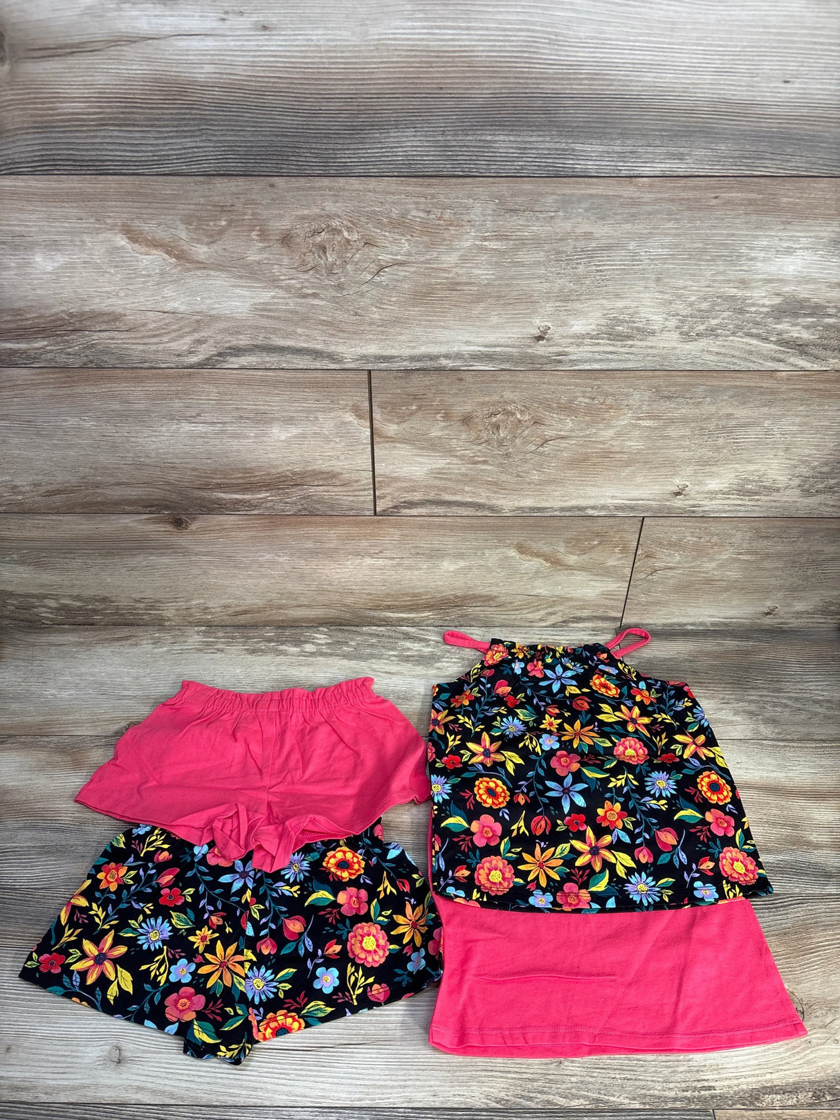 Flat lay of 4-piece girls' set: floral halter tank, floral shorts, pink ruffle shorts and pink skirt on wood background