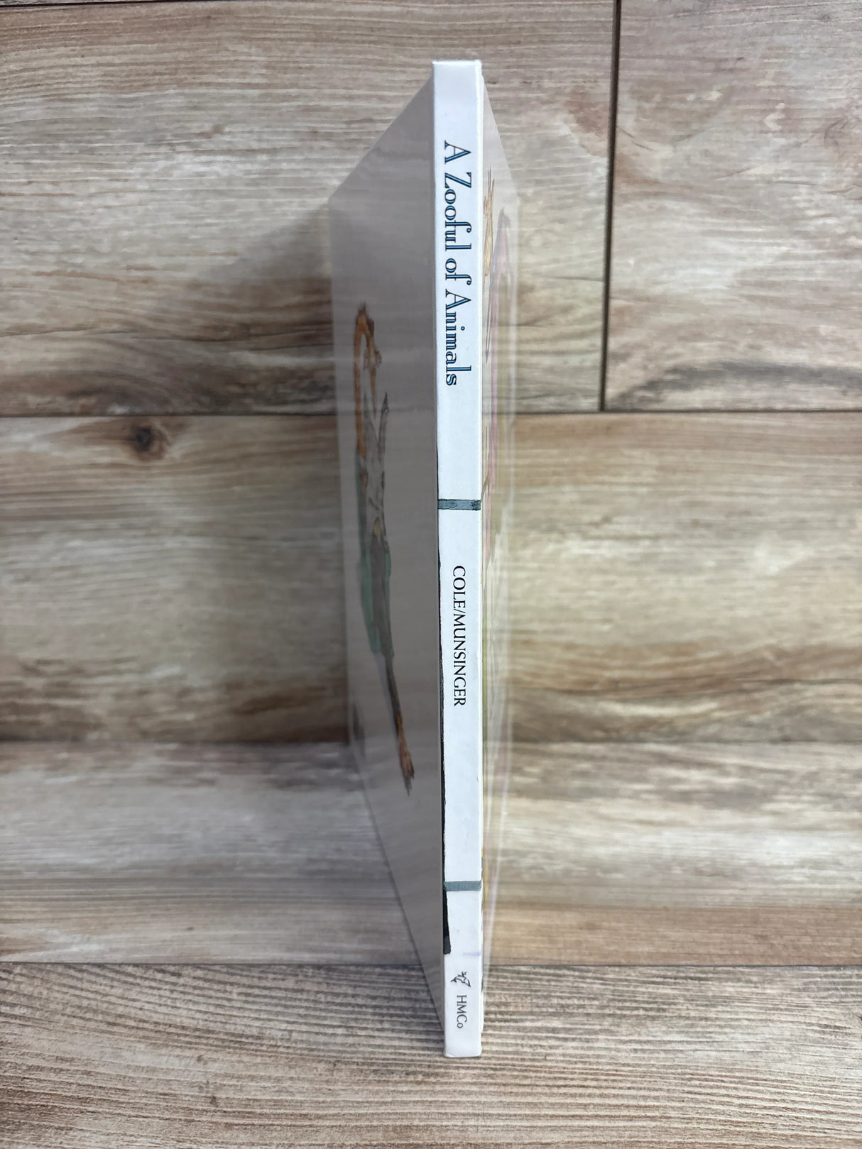 Spine view of A Zooful of Animals hardcover book by Cole and Munsinger showcasing white spine with blue title text on wood plank floor