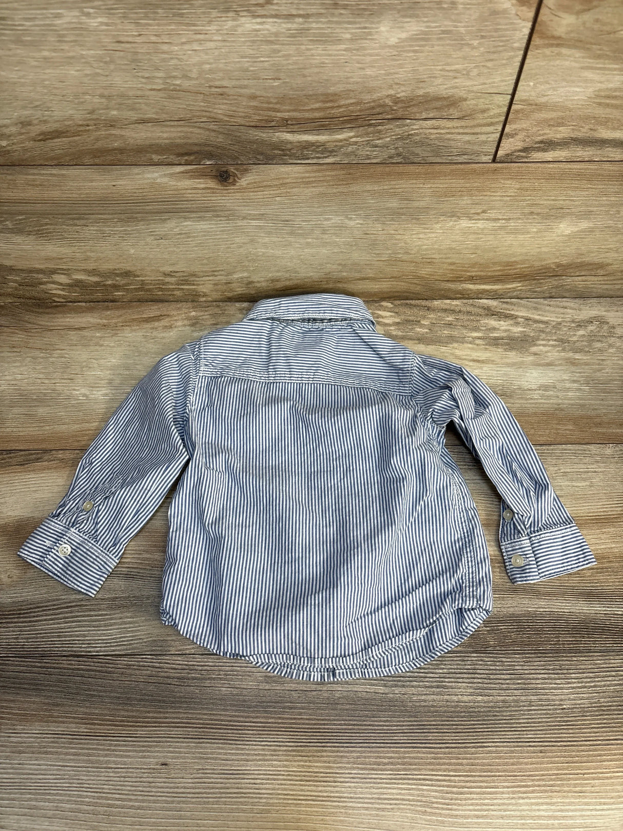 Long sleeve blue and white striped button-up toddler shirt on wood background