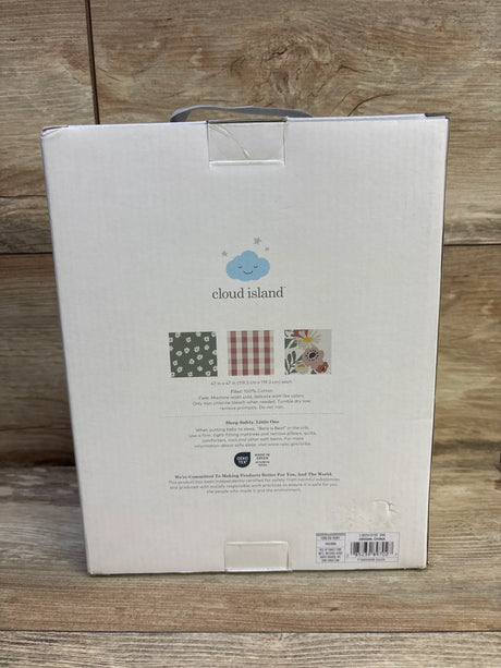 Front of Cloud Island 3-pack muslin swaddle blanket box showing three pattern thumbnails (green floral, pink gingham, and floral print) on a wooden floor background