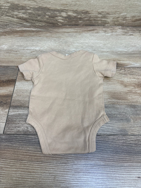 Front view of Colored Organics tan newborn bodysuit with short sleeves and rounded neckline on a wood-grain background