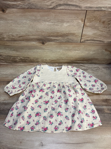 Flat lay of ivory gauze long-sleeve baby dress with pink floral print and smocked bodice on wood background, size 2T