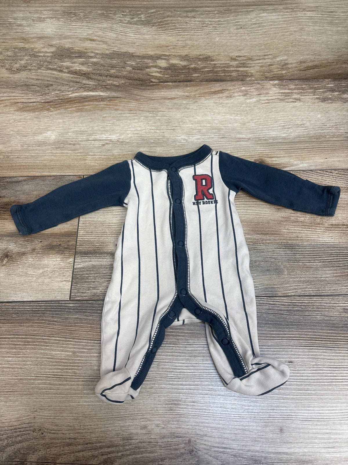 Front view of Carter’s Rookie Snap Sleeper in ivory, preemie size, with navy stripes, snap front, and footed legs on a wood floor