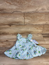 Flat-lay front of light-blue Bluey swiss-dot baby dress showing ruffled sleeves and Bluey floral print on wood background