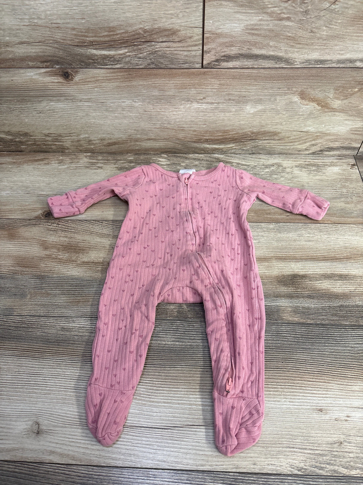 Pink footed baby sleeper with tiny heart pattern and zipper on wooden floor