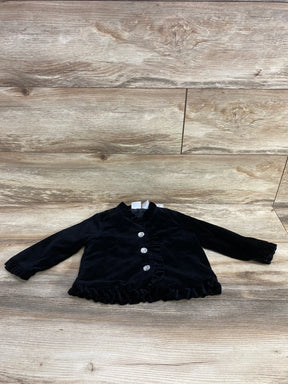 Black velvet baby jacket with ruffled edges and three decorative crystal buttons on wooden background