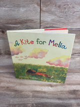 Children's book titled A Kite for Melia with colorful letters and illustration of child lying in grass under clouds