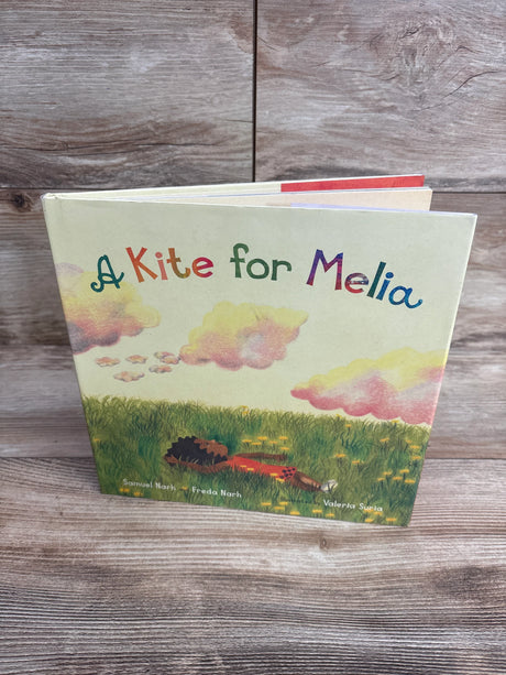 Children's book titled A Kite for Melia with colorful letters and illustration of child lying in grass under clouds