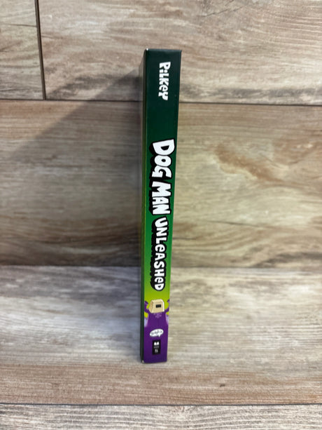Spine view of Dog Man Unleashed #2 hardcover showing green spine with white title text and purple character on wood background