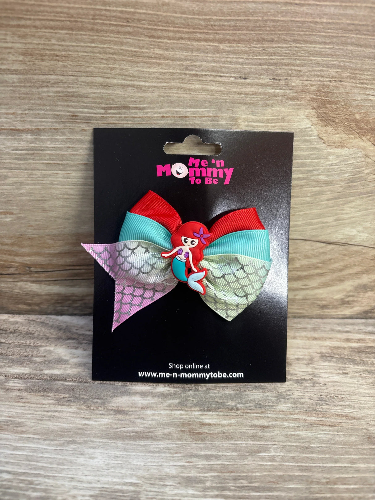 Front view of red and turquoise mermaid applique hair bow with iridescent mermaid-scale tails and mermaid charm on black card