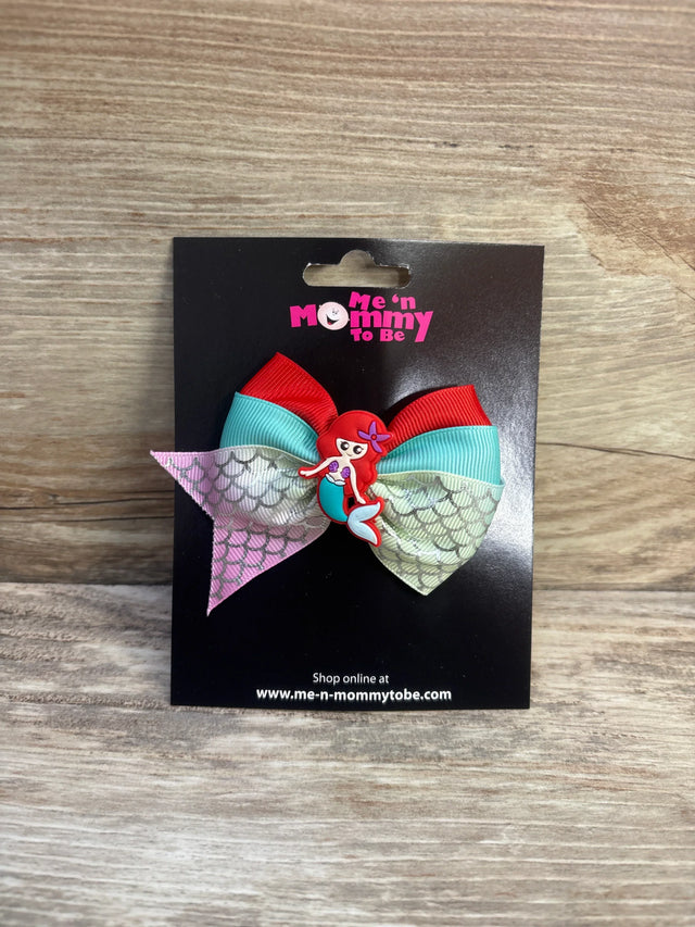 Front view of red and turquoise mermaid applique hair bow with iridescent mermaid-scale tails and mermaid charm on black card