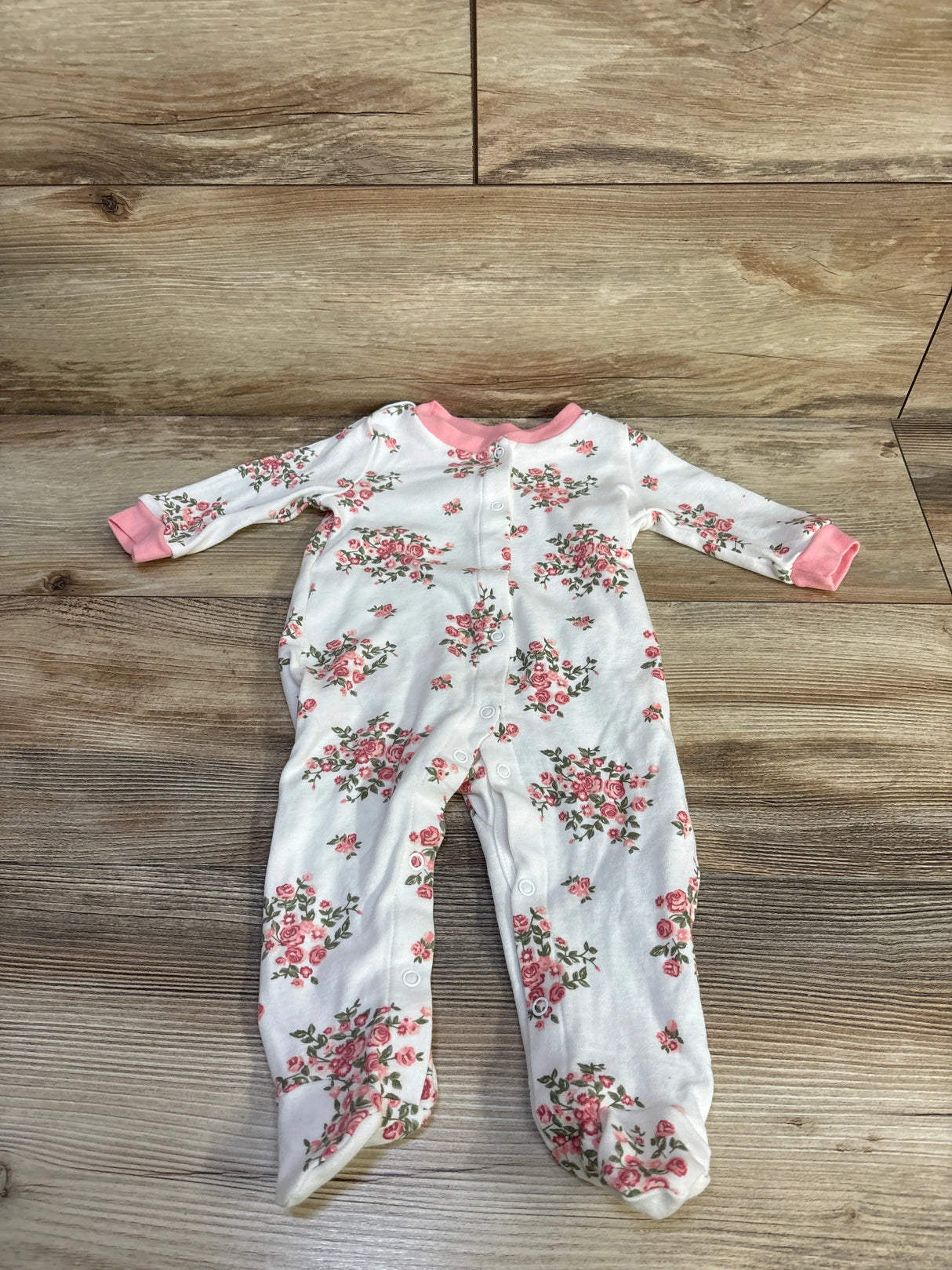 Flat lay of white floral footed baby sleeper (3-6 months) showing pink rose print and front snap closures on wood background