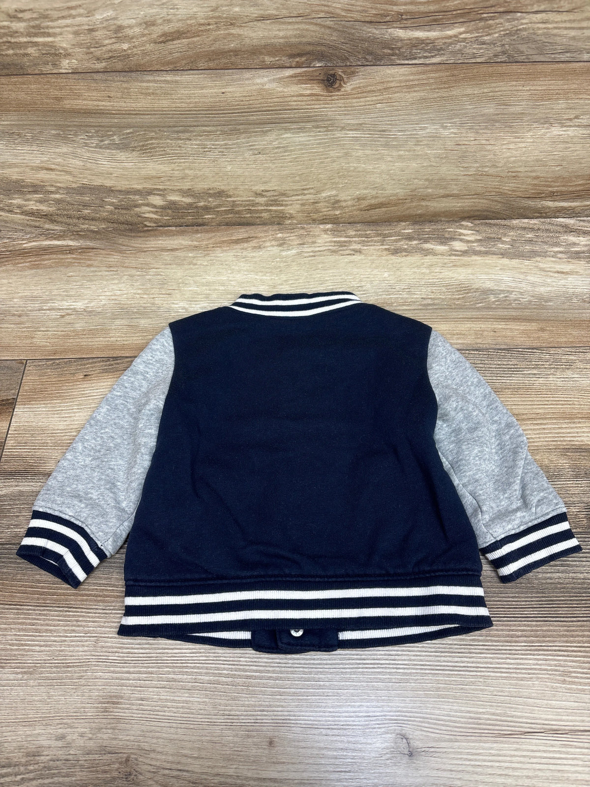 Back view of Old Navy button-front bomber jacket in navy with gray sleeves and striped ribbed trim on wooden background