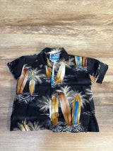 Flat lay of infant black RJC Hawaiian button-up shirt showing surfboard and palm tree print and wooden buttons on wood background