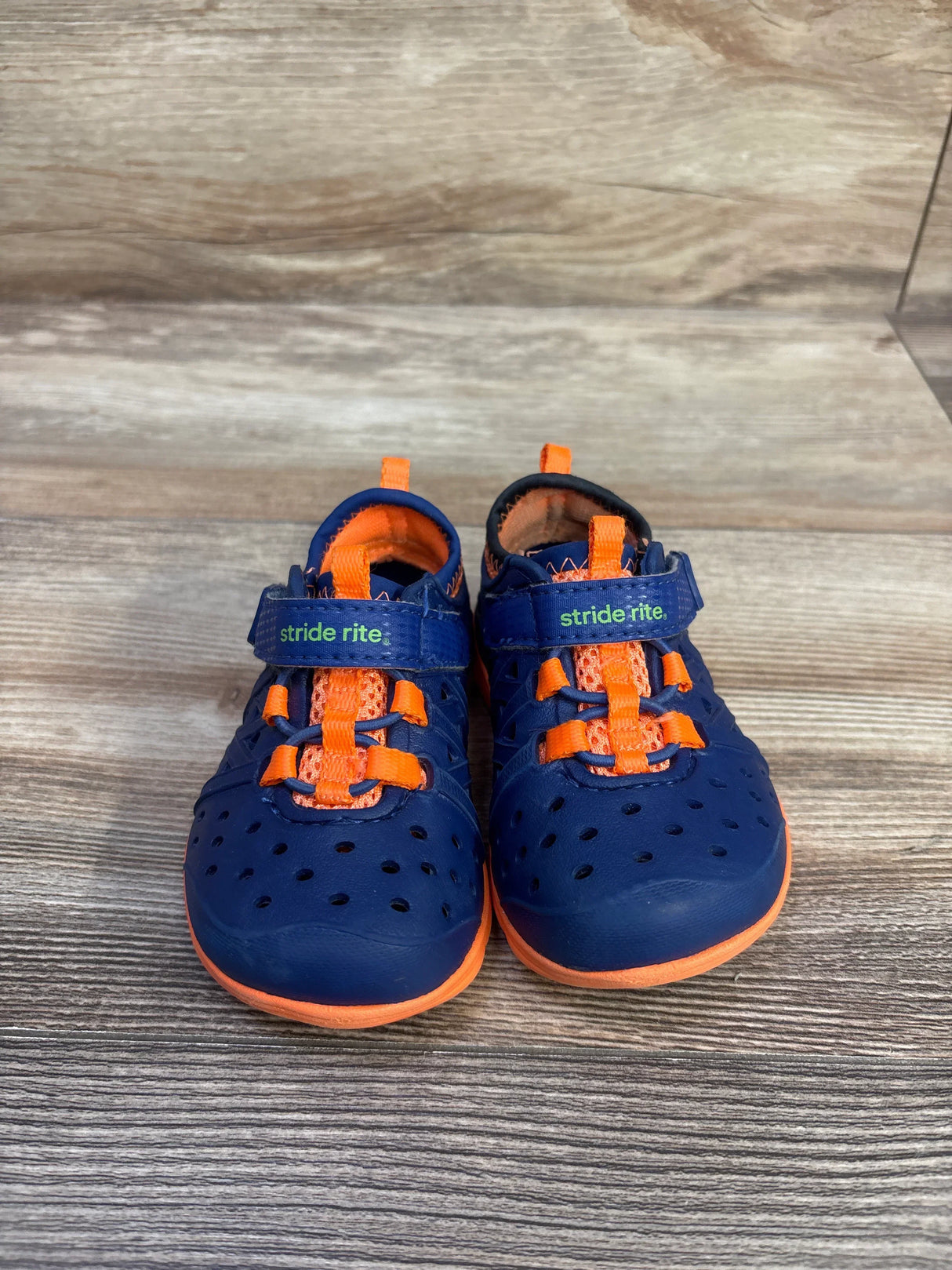 Front view of Stride Rite Phibian water sneakers, navy orange size 4C, perforated toe, bungee laces, Velcro strap on wood background