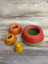 Angled view of Plantoys Cone Stacking Toy showing four colorful stackable wooden cones red, green, orange and yellow on a light wood surface