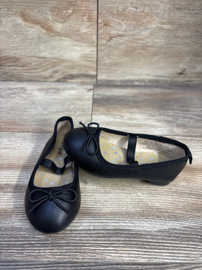 Front three-quarter view of Cat and Jack toddler black slip-on ballet flats showing elastic instep strap and bow on wood floor
