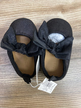 Black toddler girl shoes with large fabric bows on top, soft sole, and retail tags on wooden surface