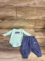 Flat lay of Nike 2-piece bodysuit and joggers showing Nike chest logo on light blue top and purple joggers on wood background