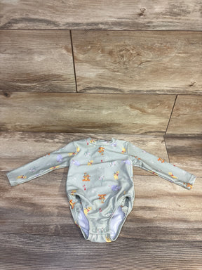Flat lay of green Winnie the Pooh rashguard swimsuit size 9M with snap crotch and all over print on wood floor
