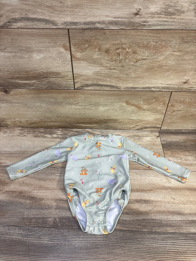 Flat lay of green Winnie the Pooh rashguard swimsuit size 9M with snap crotch and all over print on wood floor