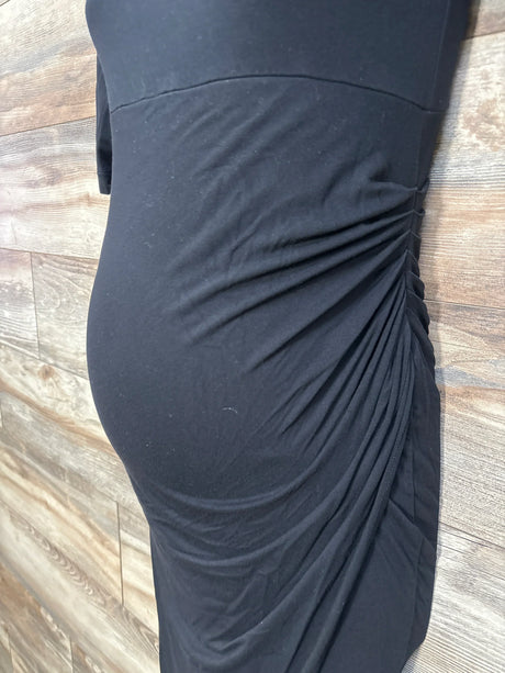 Side view of black maternity Isabella Oliver short sleeve dress showing side ruching over fitted bump panel on wood planks