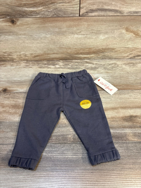 Gray baby pants with ruffled cuffs, Cat & Jack tag, and yellow 'Baby Sun' patch on wood floor