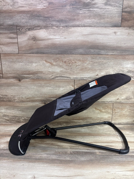 Angled view of BabyBjörn Balance Soft Bouncer in Black/Dark Grey with reclining seat, harness, and black frame on a wood-look floor