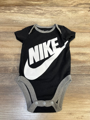 Flat lay of newborn black Nike bodysuit showing large white NIKE logo and gray trim on wood background
