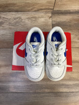 Top-down view of Nike Dunk Low toddler sneakers in white with hyper royal Swoosh, on red Nike box on wood floor