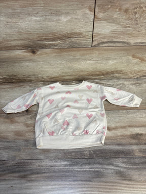 Cream long sleeve baby sweatshirt with pink and beige heart print on wood floor