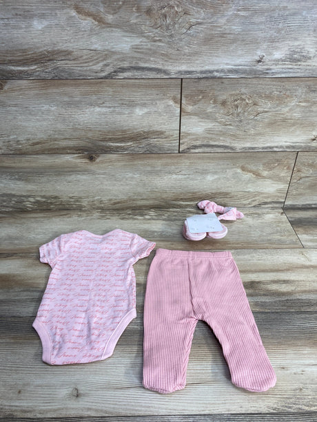 Pink baby girl outfit set with script onesie, ribbed footed pants, and matching headband on wood floor