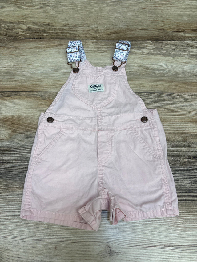 Front view of Oshkosh pink shortalls, size 18 months, with floral straps, bib pocket, and side pockets on wood grain