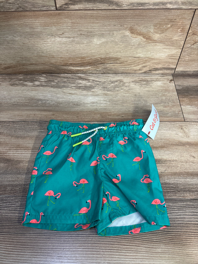 Front view of teal toddler swim trunks (12 months) with pink flamingo print, elastic waist and neon drawstring on wooden floor
