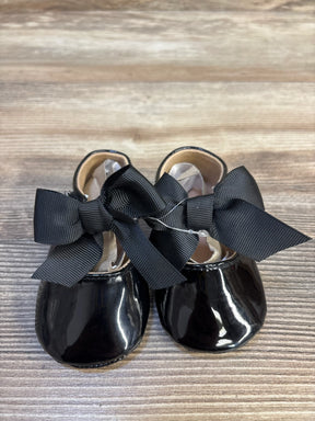Black patent baby shoes with large black bows on wood background