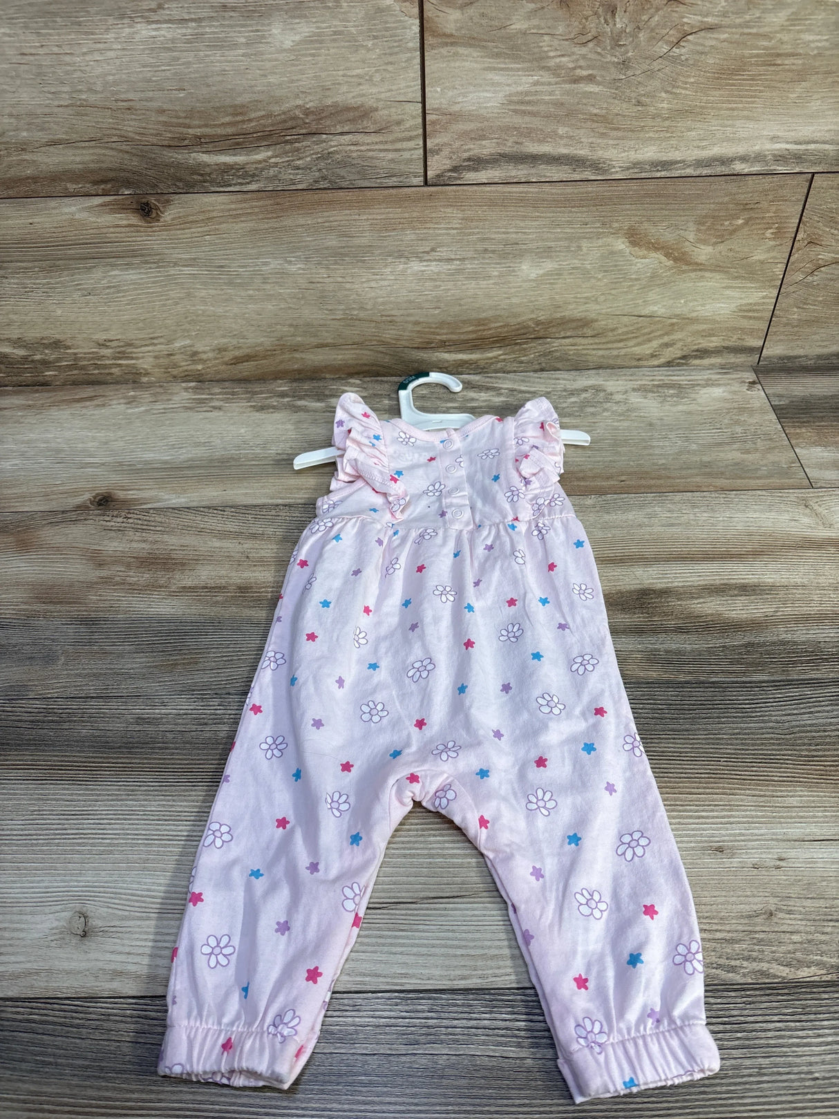 Front view of pink Bluey floral jumpsuit size 0-3m with ruffle cap sleeves and flower and star print on wood background