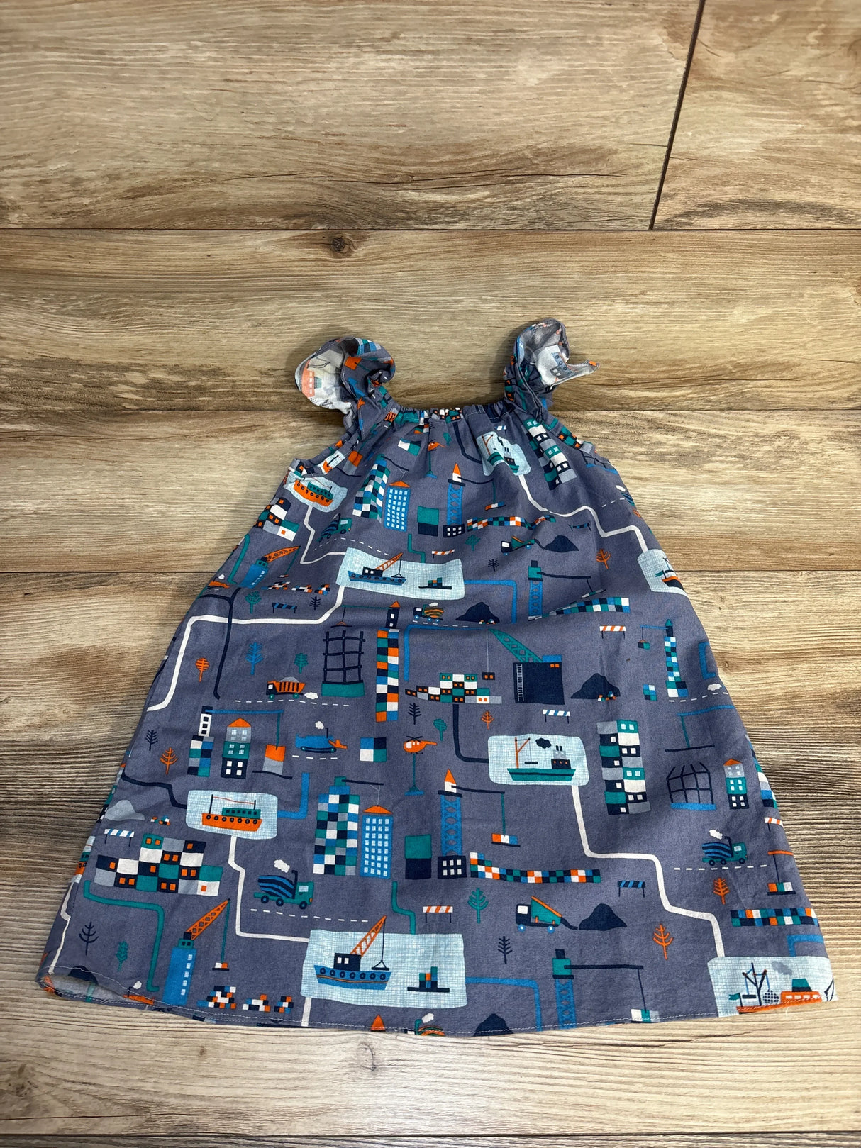 Gray baby dress with city map print, construction trucks, boats, and buildings on wood floor