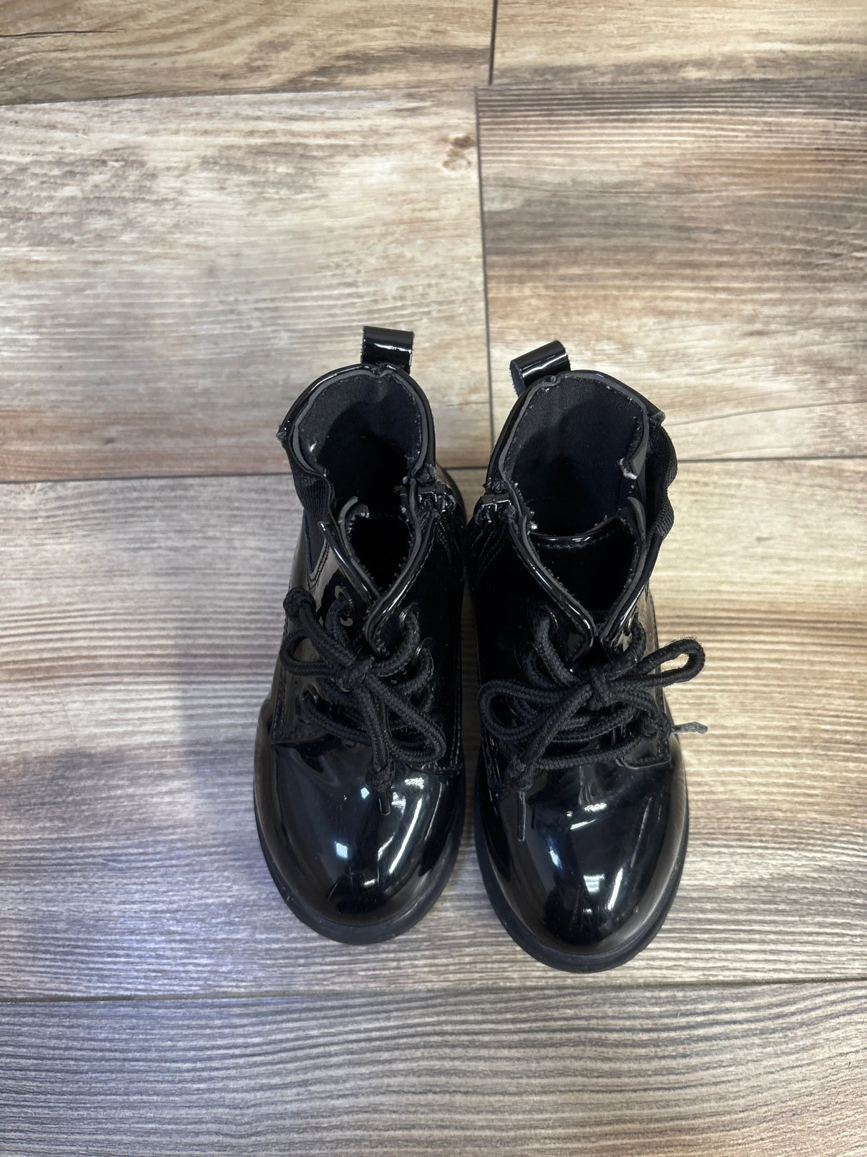 Top-down view of Comfy Kids faux leather lace-up boots size 8C with glossy black finish and laces on wood floor