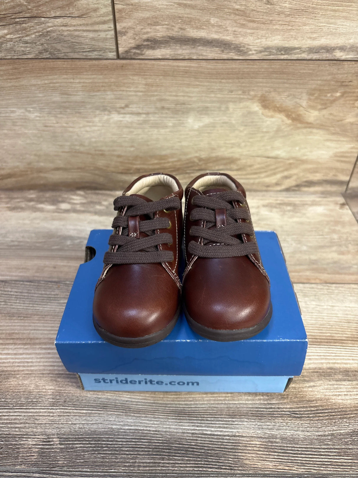 Front view of Stride Rite SRTech Elliot toddler sneakers in brown leather showing lace-up design and contrast stitching on a blue Stride Rite box