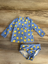 Flat lay of 2-piece blue lemon-print rashguard and bikini bottoms showing long sleeves and yellow lemons on wooden floor